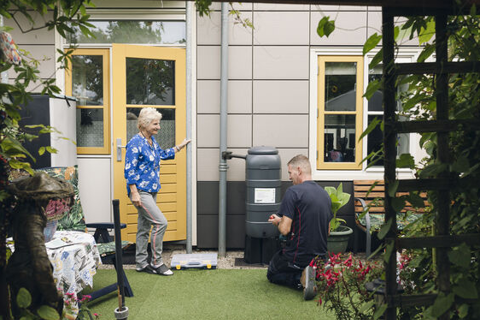 Vrouw staat bij regenton met een vakman.