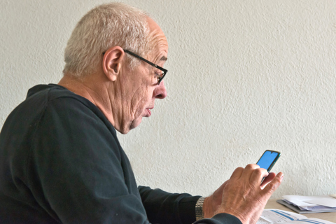 Foto van oude man kijkt verbaasd naar mobiele telefoon