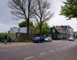 Foto van straat met twee mensen die kijken naar een leeg plot grond